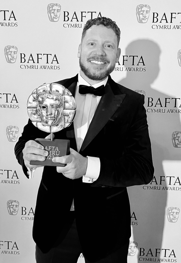 Ein Mann in einem Smoking, der eine BAFTA-Trophäe hält und lächelt, vor einem Hintergrund mit der Aufschrift "BAFTA Awards 2018."