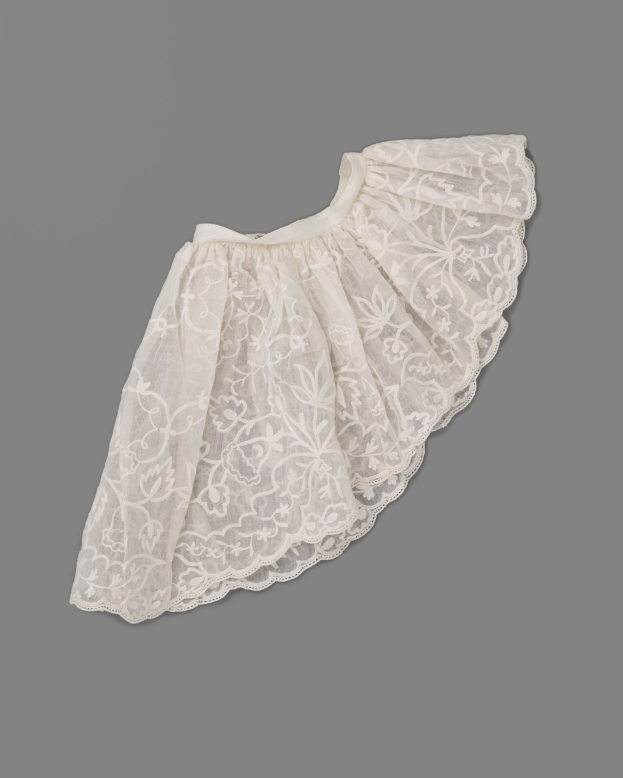 Weißer Rock mit zartem Spitze-Überzug auf grauem Hintergrund, mit leichtem Stoff und feiner kleiner Stickmuster.