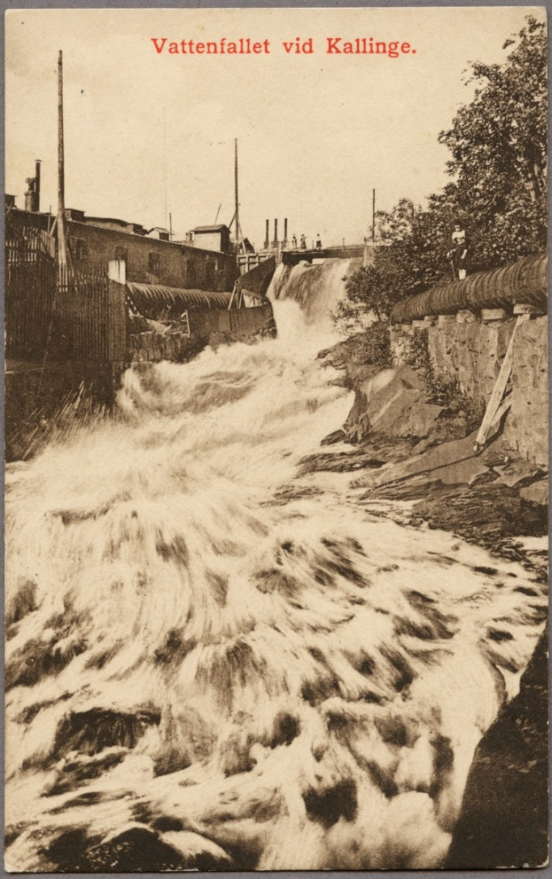 Altes Schwarz-Weiß-Foto eines Flusses mit fließendem Wasser, Bäumen, Gebäuden, Strommasten, einem Zaun und Text oben.