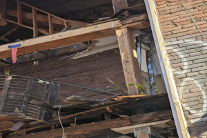 Ein teilweise abgerissener Bau mit verstreuten Holzplanken und Trümmern, mit gebrochenen Fenstern und Türen.