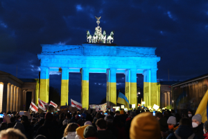 Eine Menschenmenge steht vor dem Brandenburger Tor in Berlin, Deutschland, mit Fahnen und Schildern in den Händen.