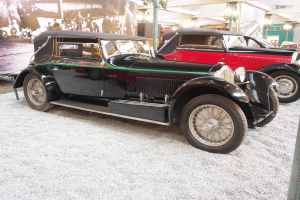 Eine Gruppe von Oldtimern in einem Museum ausgestellt, mit einem Banner auf der linken Seite, das Fotos von Menschen und Text zeigt, und an der Decke angebrachten Lichtern im Hintergrund.