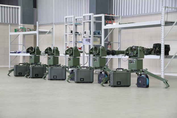 Gruppe von Militärrobotern auf einem Boden mit Koffern und Gegenständen auf Gestellen, in der Nähe einer Wand und eines Geländers als Teil eines Verteidigungsystems positioniert.