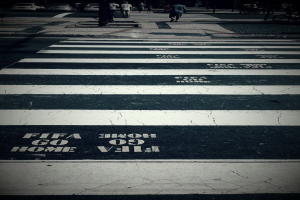 Menschen gehen über eine Zebrastreifenübergang, während Autos in der oberen linken Ecke sichtbar sind.
