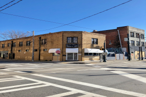 Eine leere Straße mit einem Zebrastreifen vor einem Backsteingebäude an der 541 W 5th St, Chicago, gesäumt von Laternenmasten, Brettern und Bäumen, unter einem sichtbaren Himmel.