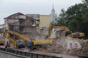 Eine belebte Abrissszene in Kiew, Ukraine, mit Kränen, Fahrzeugen, Menschen und diversem Schutt sowie einem sichtbaren Himmel und einem Wasserzeichen.