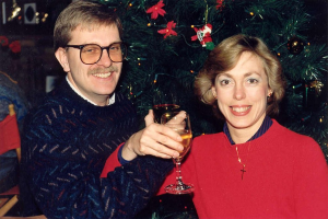 Ein Paar lächelt, waßrend es Gläser mit Wein hält, mit einem Weihnachtsbaum im Hintergrund.