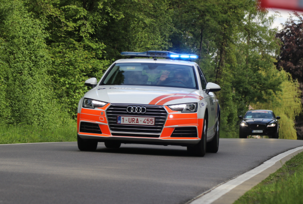 Ein Polizei-Audi A4 mit zwei Insassen auf einer grasbewachsenen Straße neben einem Wald unter einem klaren blauen Himmel.