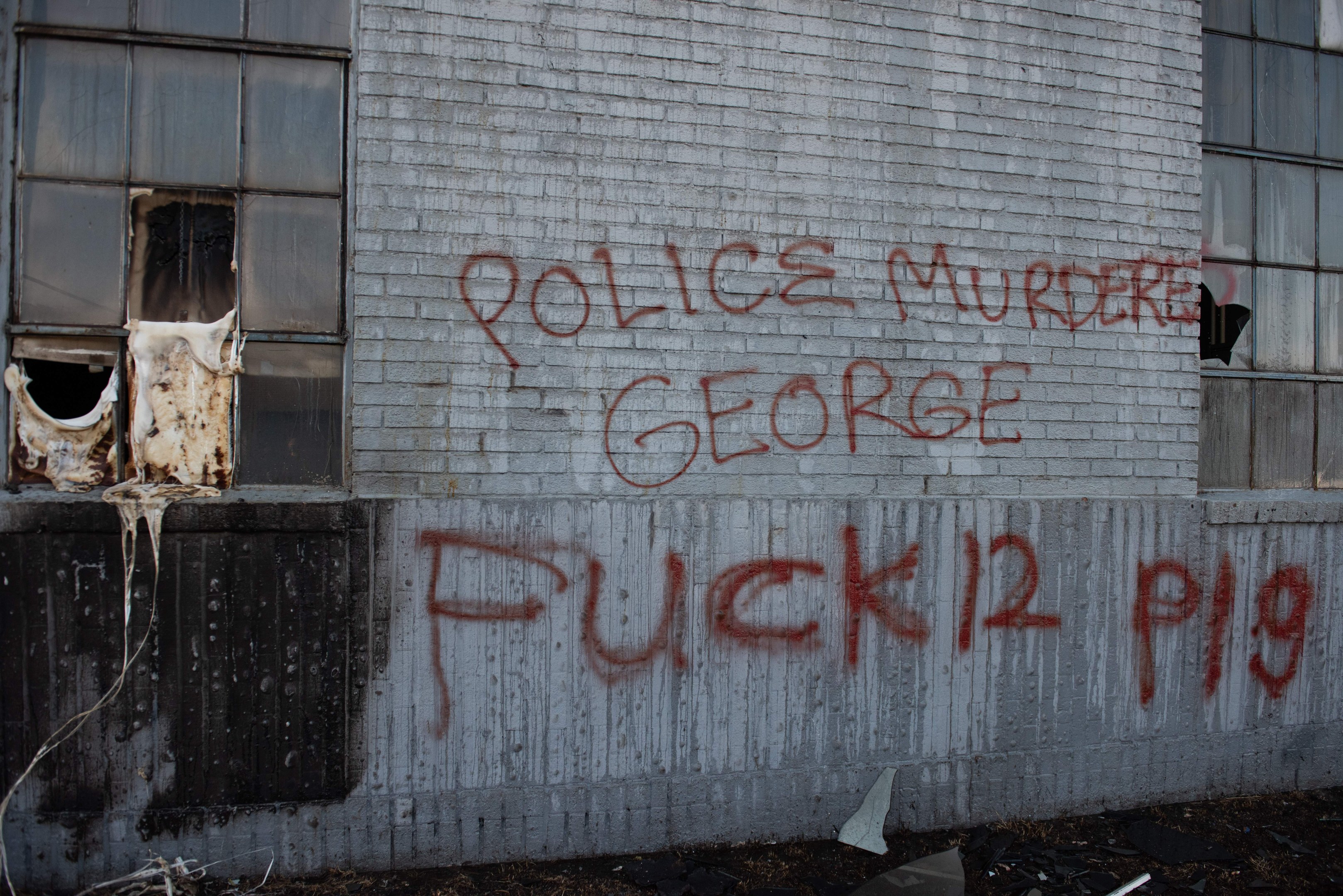 Graffiti an einer Hauswand mit der Aufschrift "Polizei Mord George Fuck 12 P19" mit Fenstern und verstreuten Gegenständen davor.