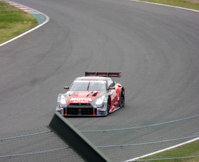 Ein Nissan GT-R Nismo GT3 Rennauto auf der Nürburgring 24 Stunden Strecke mit grünem Gras auf beiden Seiten.