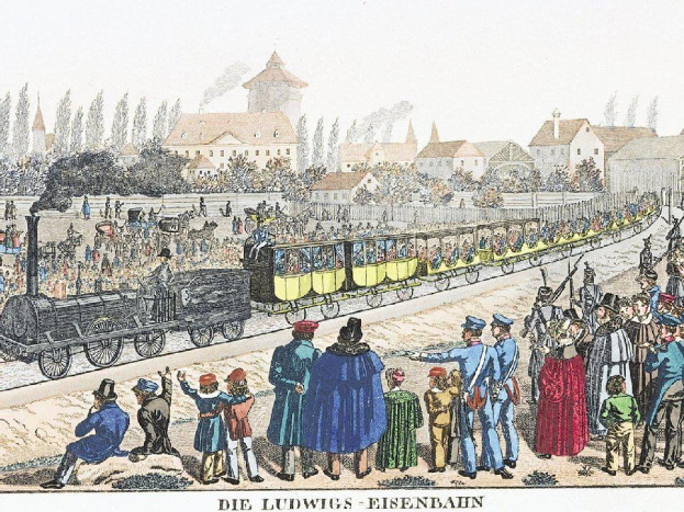 Eine Gruppe von Menschen steht um einen Zug auf einem Gleis, einige sitzen im Zug, andere stehen daneben, in der Nähe von Gebäuden und Bäumen, mit dem Text "Ludwigs-Eisenbahn, der erste Bahnhof in Deutschland" unten.